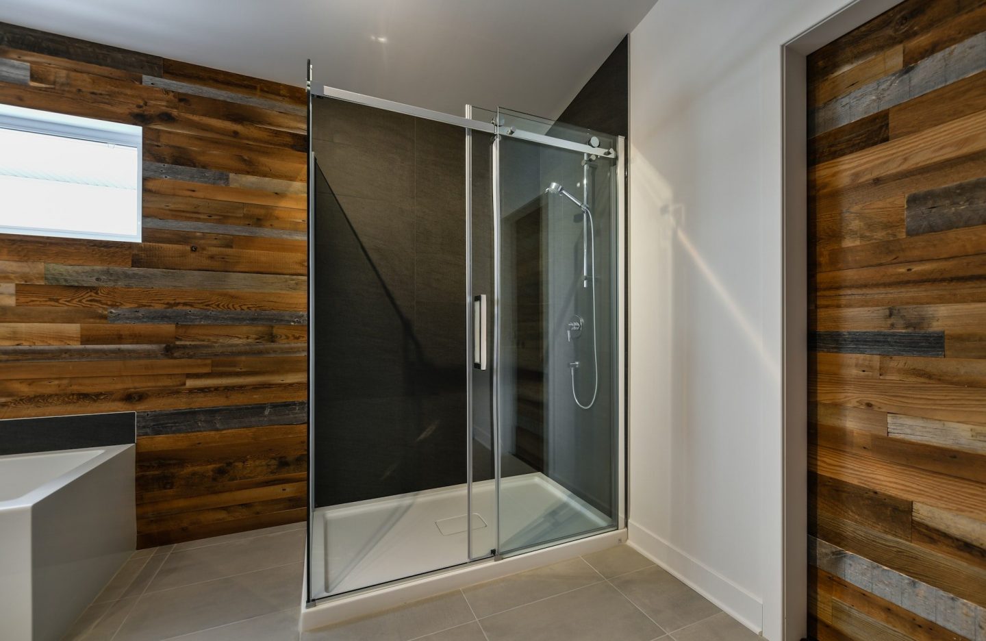 A modern bathroom with wood walls and a glass shower stall.