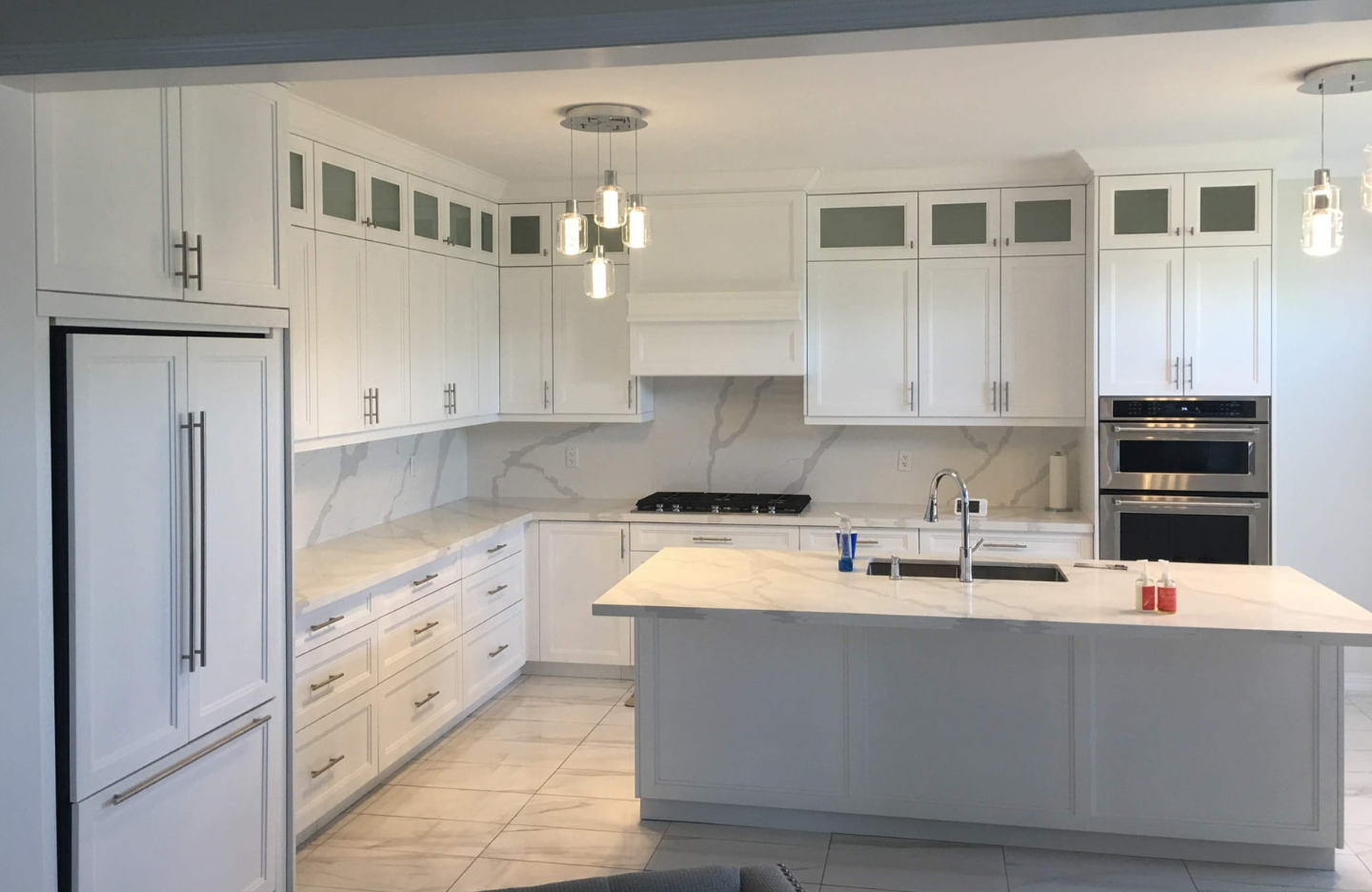 A kitchen with white cabinets and marble counter tops.