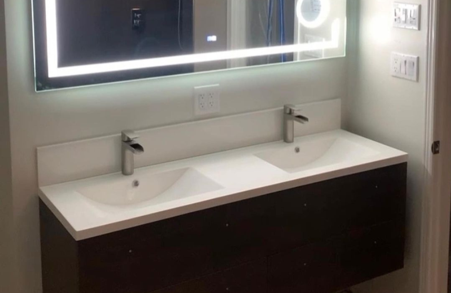 A bathroom with two sinks and a lighted mirror.